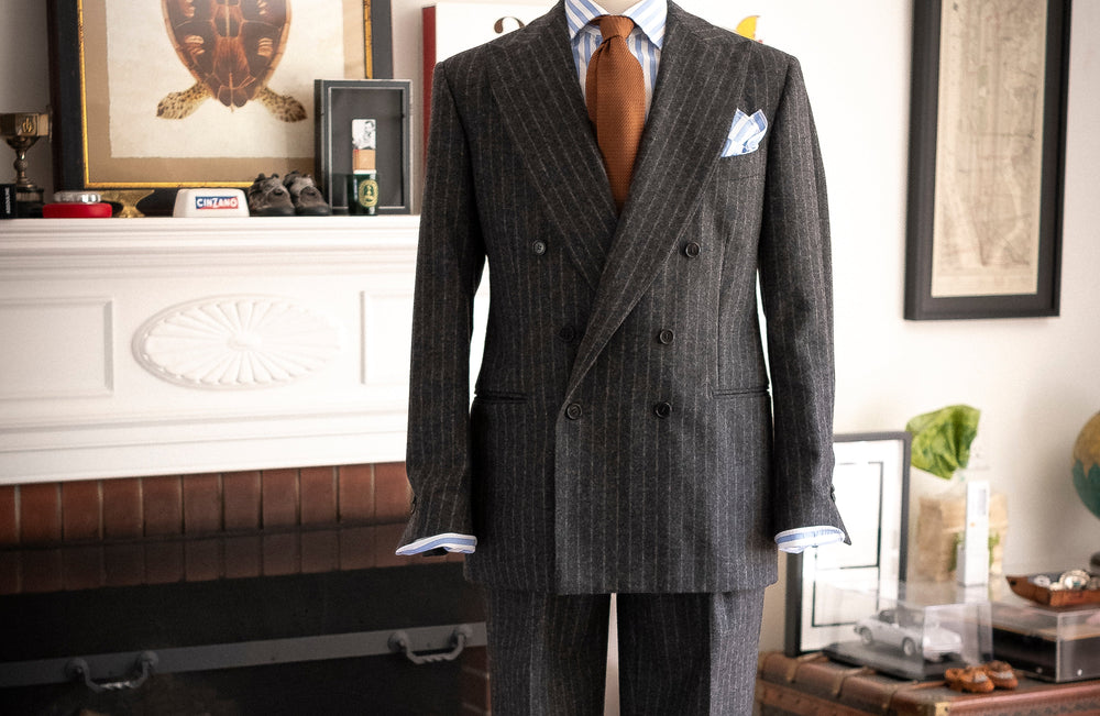 Gray pinstripe suit on a mannequin in a room with a fireplace and framed pictures.